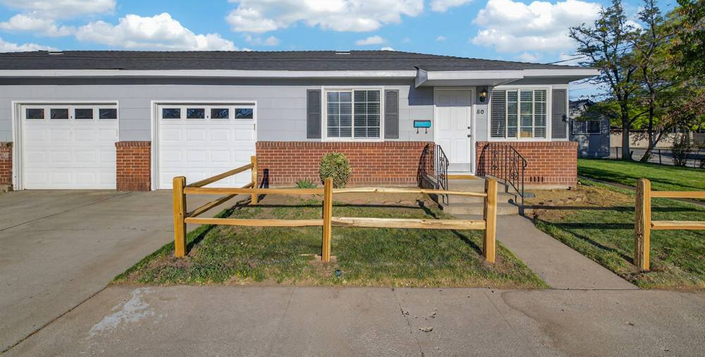 The duplex from the street: single storey, two attached garages, red brick base and a split-rail fence around the lawn