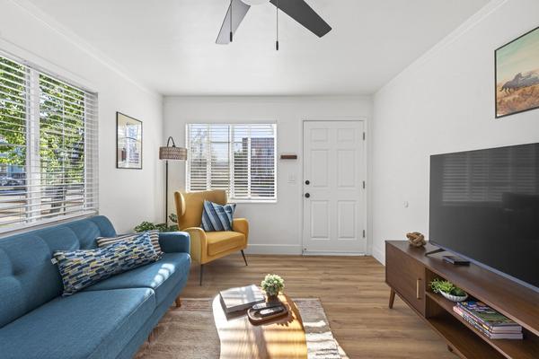 Living room with a teal sofa, a mustard armchair, a large TV on a walnut media console and the front door in the corner