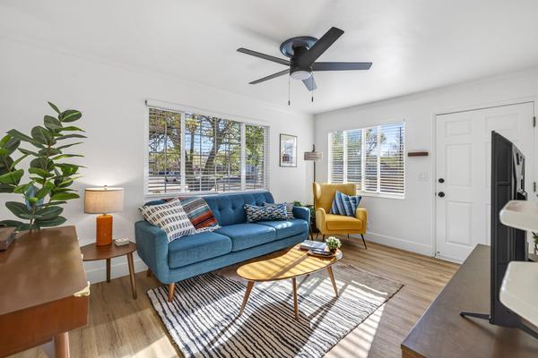 Living room corner with the teal sofa, an oval wood coffee table on a striped rug and windows on two walls