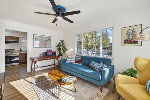 Living room looking toward the kitchen doorway, with a walnut writing desk under a framed print and a ceiling fan