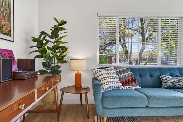 Walnut desk with a record player and an orange table lamp beside the sofa, under a wide window