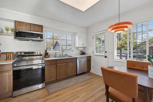 Kitchen with walnut cabinets, a stainless range and microwave, a dishwasher, and a dining table under an orange pendant light