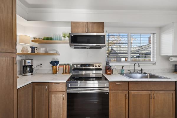 Kitchen run with an electric range, open wood shelves of dishes and glasses, a coffee maker and a window over the sink