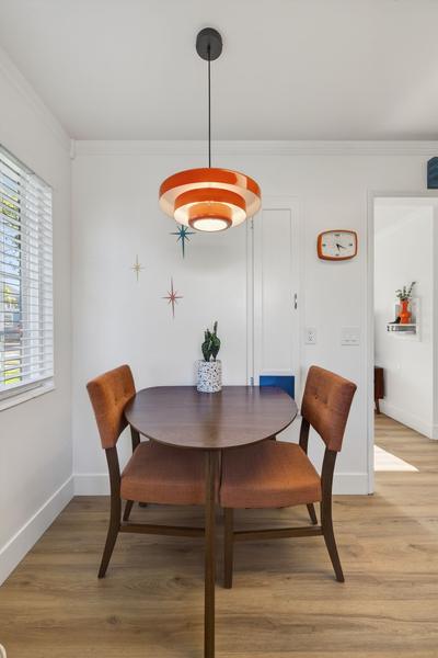 Round walnut dining table and two orange upholstered chairs under an orange saucer pendant