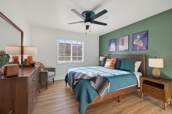 Bedroom with a queen bed in teal bedding, a sage green accent wall with three motel sign prints, walnut nightstands and a dresser