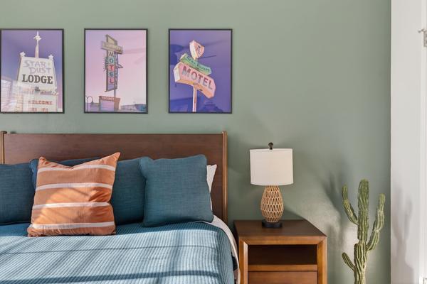 Headboard wall: teal and orange pillows, a nightstand lamp and three framed vintage Reno motel sign prints
