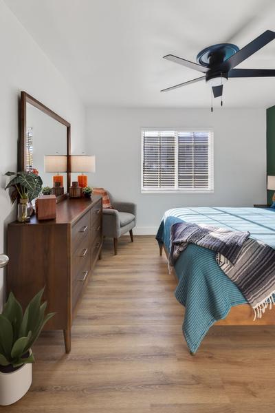 Walnut dresser with a mirror and lamps, a grey armchair by the window and the foot of the bed