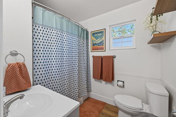 Bathroom with a patterned shower curtain, orange towels, a framed print and a window