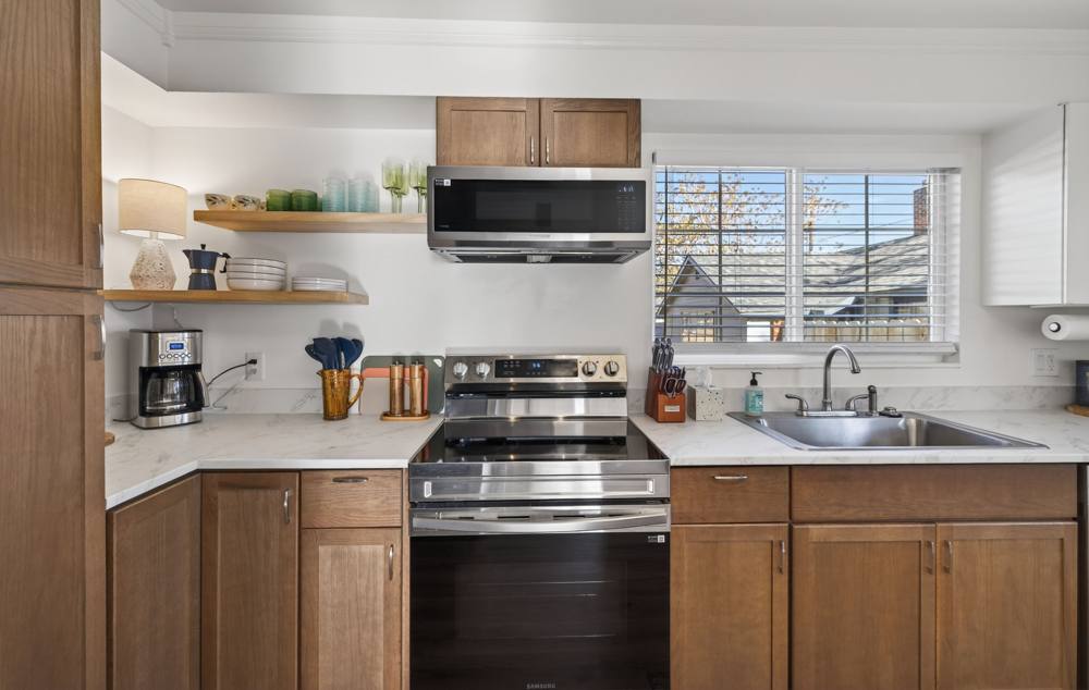 Full kitchen with walnut cabinets, electric range, open shelving and a window over the sink