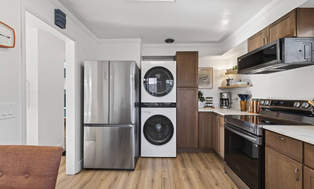 Full-size stacked washer and dryer built into the kitchen run beside a stainless steel refrigerator
