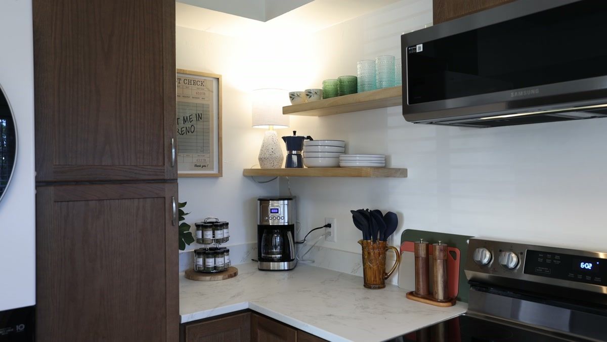 Kitchen corner with open shelving, a coffee maker, stacked bowls and glassware beside the range