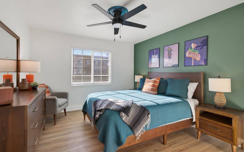 Bedroom of 80 Locust: queen bed against a sage green wall hung with vintage Reno motel sign prints, walnut dresser and nightstands